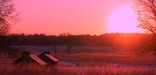 The sun rising over a snowy expanse containing two huts.